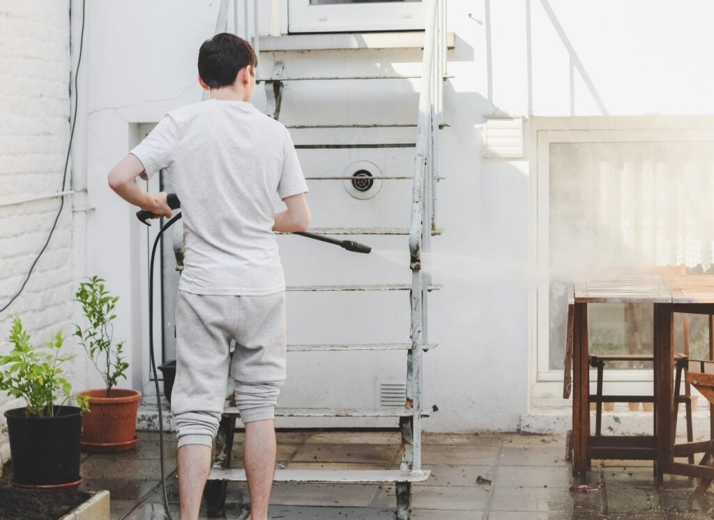 A caucasian guy in gray sports and a T-shirt from the back washes metal a ladder up